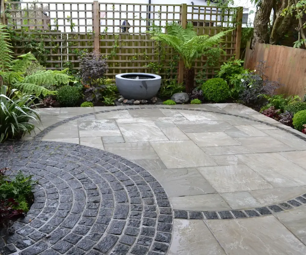A new stone patio with a curved cobble border and planted borders